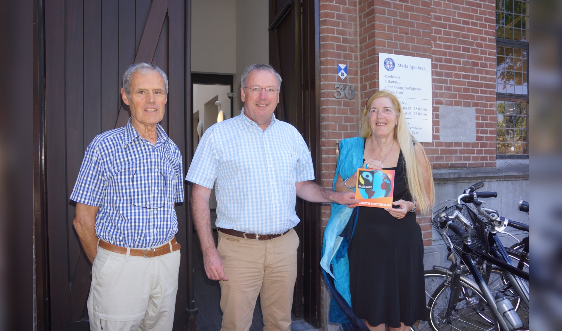 Piet van Berkel en Marianne Bruin - van Groningen overhandigen het Fairtrade bordje aan John ten Ham (midden) van de apotheek.