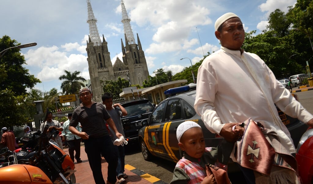 Moslimgelovigen op weg naar de Istiqlalmoskee in Jakarta met op de achtergrond de rooms-katholieke kathedraal. (beeld AFP / Romeo Gacad)