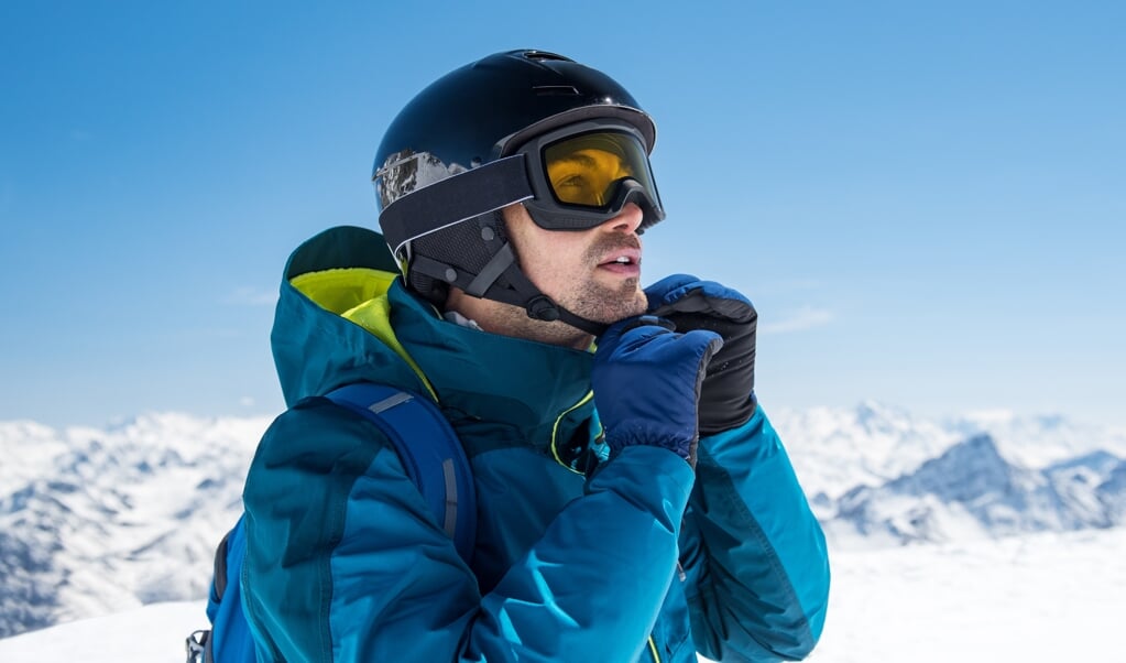 Man skier wearing helmet and ski mask on snowy mountain. Man getting ready for a ski trip in winter. Young skier looking at mountain covered by snow. (beeld Getty Images/iStockphoto)