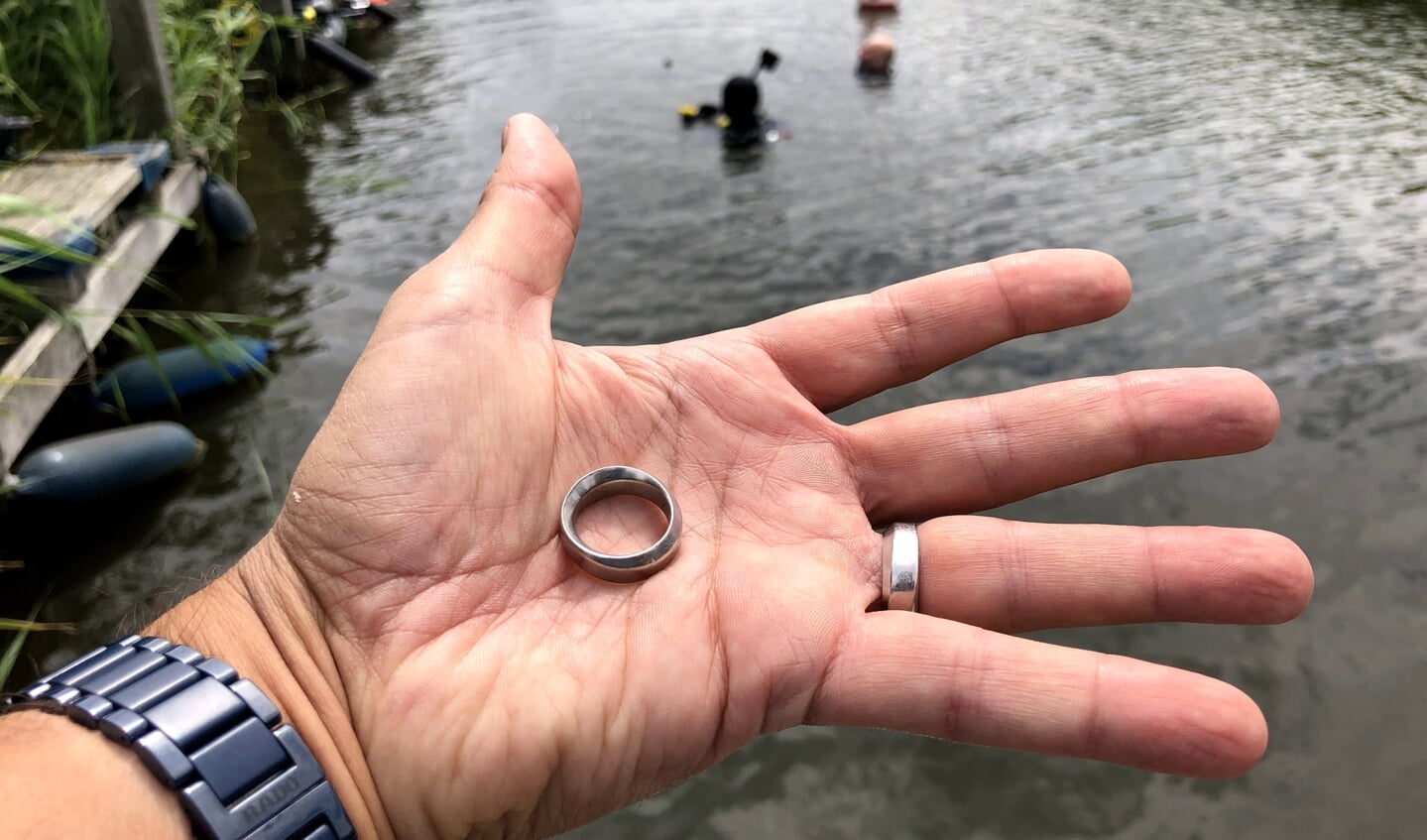 Deze ring werd opgedoken. Op de achtergrond de duiker die de ring gevonden heeft.