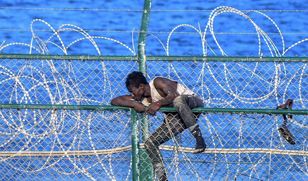 Een man probeert over het grenshek te klimmen en uit handen van de grenspolitie te blijven. (beeld afp / Antonio Sempere)