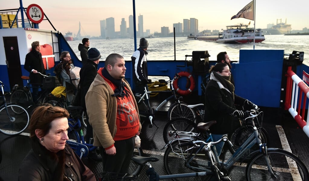 Fietsers en voetgangers op de tijdelijke pont over de Maas in Rotterdam. Aan de horizon de Erasmusbrug en de Kop van Zuid. (beeld Marcel van den Bergh)