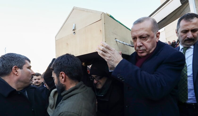 De Turkse president Erdogan draagt de kist van een slachtoffer van de aardbeving tijdens een bezoek aan het getroffen gebied zaterdag. (beeld afp / Murat Cetinmuhurdar)