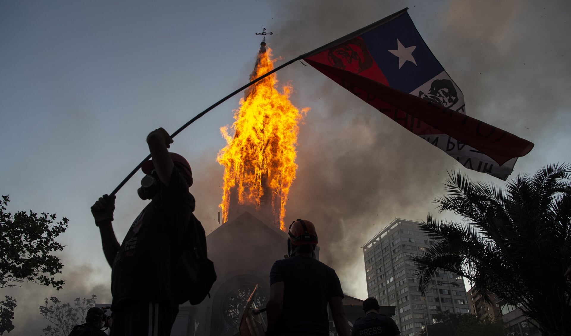 Een actievoerder met de Chileense vlag bij de brandende toren van de kerk van Asuncion in Santiago, Chili. 