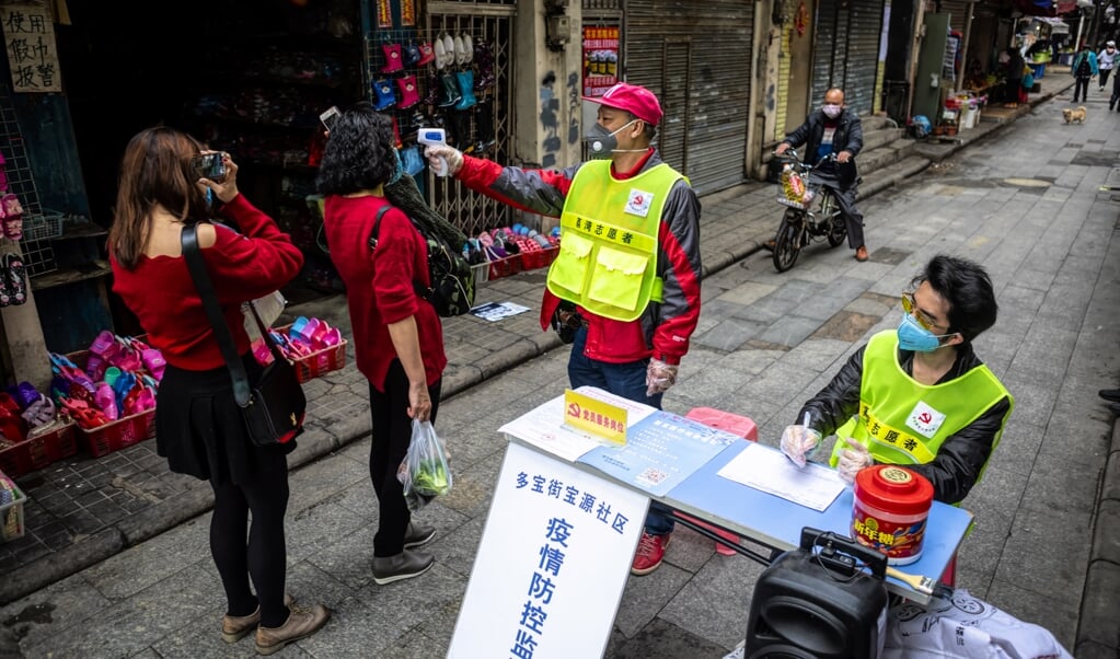 Een man meet de lichaamstemperatuur van mensen bij een wegversperring in Guangzhou in China in de strijd tegen de verspreiding van het coronavirus. (beeld epa / Alex Plavevski)