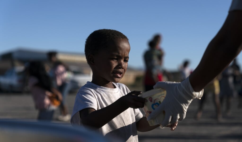 Een Zuid-Afrikaanse jongen in Kaapstad krijgt voedsel uitgereikt. Inwoners die niet kunnen werken door de lockdown, krijgen nu ook een geldbedrag. (beeld epa / Nic Bothma)