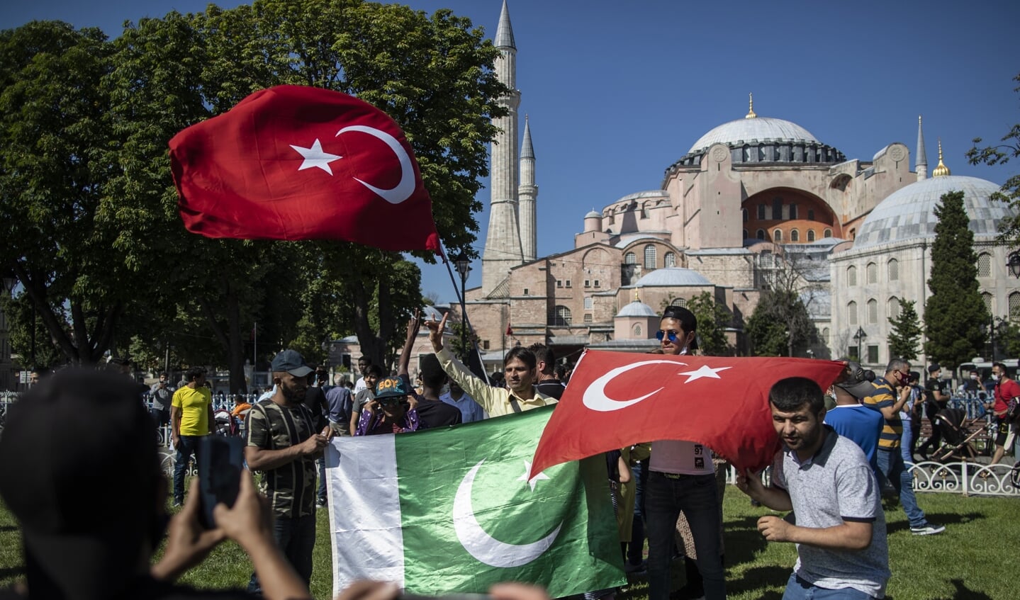 Mensen zwaaien met Turkse en Palestijnse vlaggen, om de beslissing te vieren dat de Hagia Sophia (op de achtergrond) weer moskee wordt