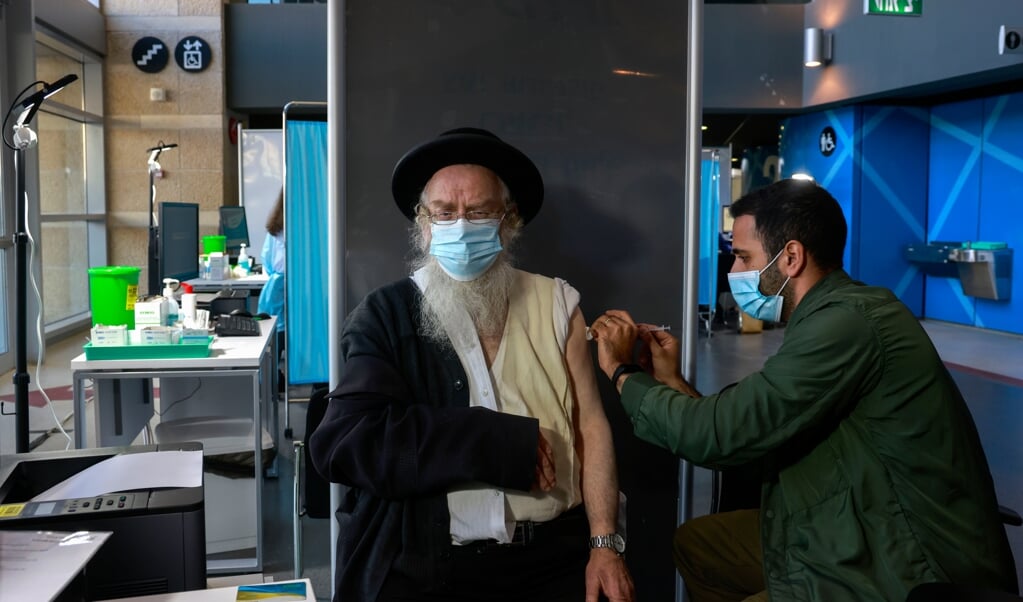 Een zorgmedewerker vaccineert een man bij de Israëlische Clalit Health Services in Jeruzalem. (beeld afp / Menahem Kahana)