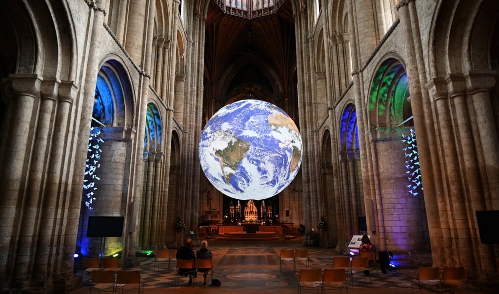 Een zeven meter grote aarde van de Britse artiest Luke Jerram in de kathedraal van Ely. Maar de lichtblauwe planeet wordt donkerder, door afname van het wolkendek. (beeld afp / Oli Scarff)