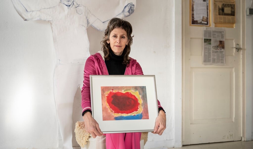 Jeannette Eisses met het schilderij dat ze twintig jaar geleden maakte: een rode wolk - die een baarmoeder verbeeldt - met daaromheen blauw, roze, geel en grijs.  (beeld Martin Waalboer)