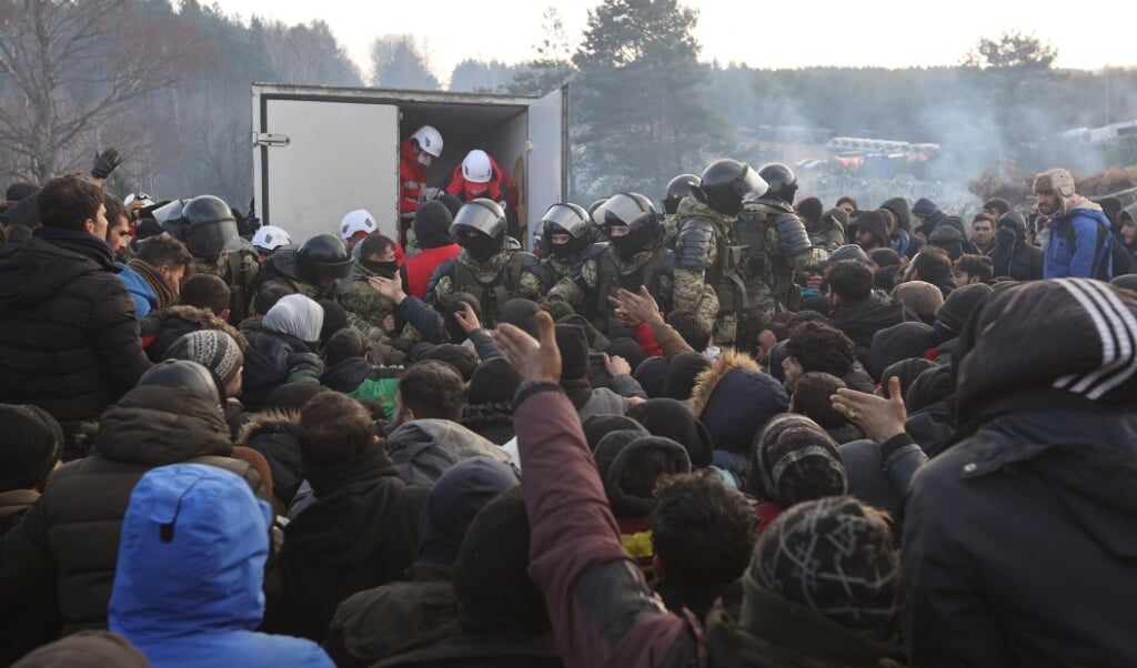 Migranten aan de grens tussen Belarus en Polen krijgen humanitaire hulp. Het vriest in dit gebied. Aan beide kanten van de grens staan troepen, waardoor de migranten geen kant op kunnen.  (beeld Ramil Nasibulin / Belta / afp)
