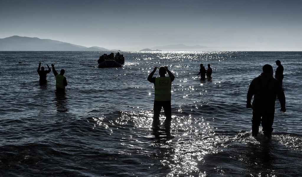 Leden van de hulporganisatie Emergency Response Centre International (ERCI) gebaren naar migranten in een bootje op zee die bijna aankomen op Lesbos. (beeld afp / Aris Messinis)