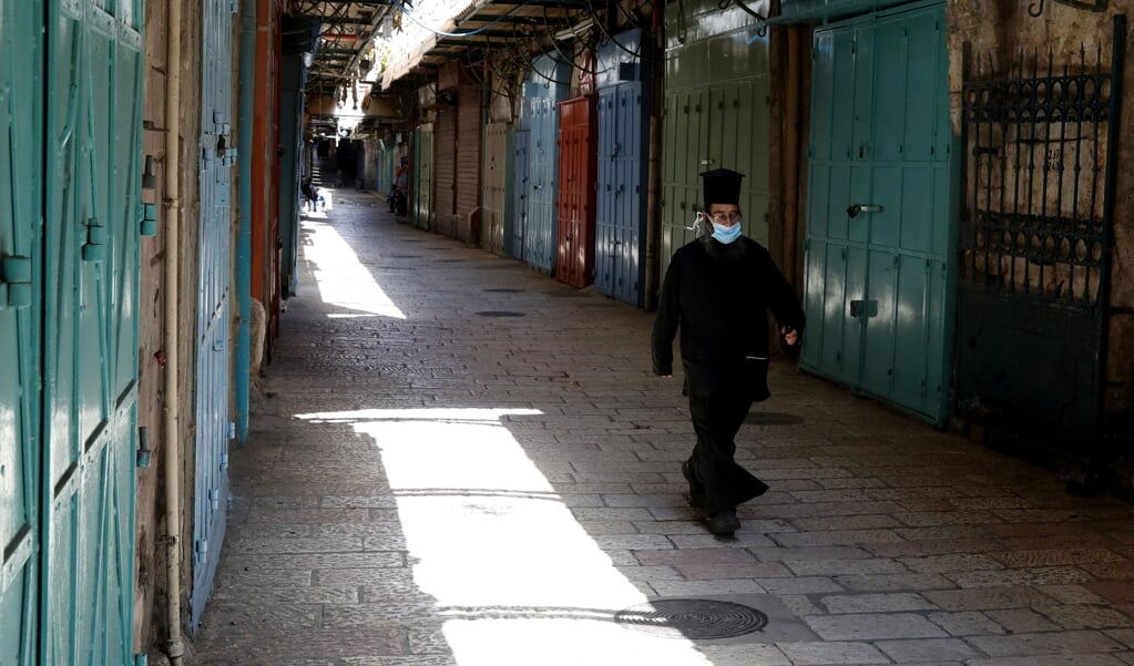 Een Grieks-orthodoxe priester loopt gemaskerd in een lege straat in de christelijke wijk in de Oude Stad van Jeruzalem. (beeld afp / Gali Tibbon)