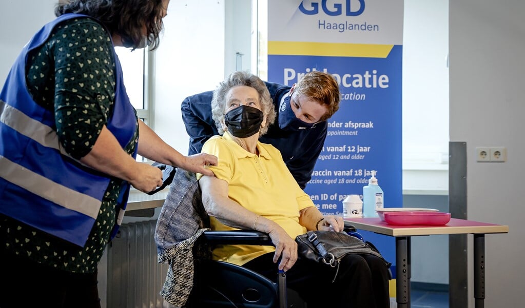 Een GGD-medewerker zet de eerste boosterprik bij een 90-jarige Haagse vrouw. Ouderen, inwoners van zorginstellingen en zorgpersoneel met direct patientencontact kunnen een boosterprik tegen het coronavirus krijgen.  (beeld anp / Robin van Lonkhuijsen)