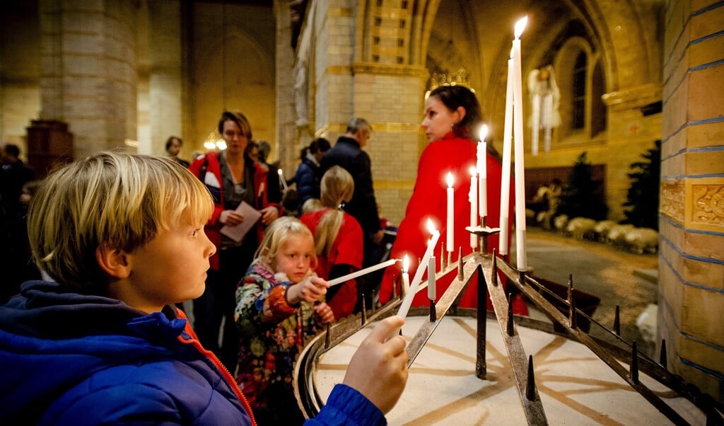 Bezoekers branden een kaarsje tijdens de kerstviering voor gezinnen met kinderen in de Kathedrale Basiliek Sint Bavo, een viering van woord en gebed rondom het kerstverhaal.  (beeld anp / Robin van Lonkhuijsen)