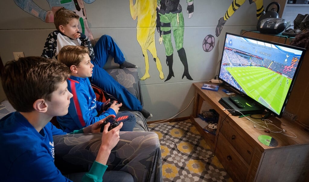 Willem-Jan en Caspar Bleijie spelen FIFA 2021 achter hun Play Station. Hun jongste broer Lennart mag toekijken. (beeld Hielco Kuipers)