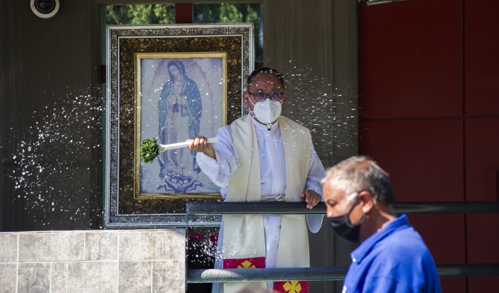 Een priester met mondkapje zegent de gelovigen in Mexico-Stad. Steeds minder Mexicanen noemen zich rooms-katholiek.  (beeld afp / Claudio Cruz)
