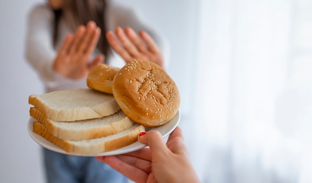 Young woman suffers from a gluten. Gluten intolerant and Gluten free diet concept, Real people. Copy space. Gluten intolerance and diet concept. Woman refuses to eat white bread. Selective focus on bread (Young woman suffers from a gluten. Gluten into  (beeld istock)