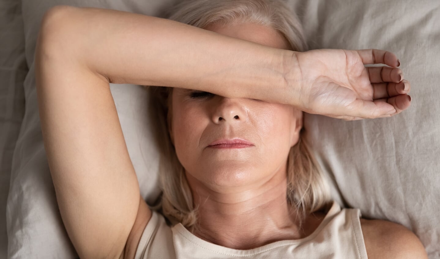 Close up top view middle-aged woman lying down in bed on pillow put hand on face, concept of female having insomnia sleeping disorder or migraine pain, melancholic mood, personal life troubles concept