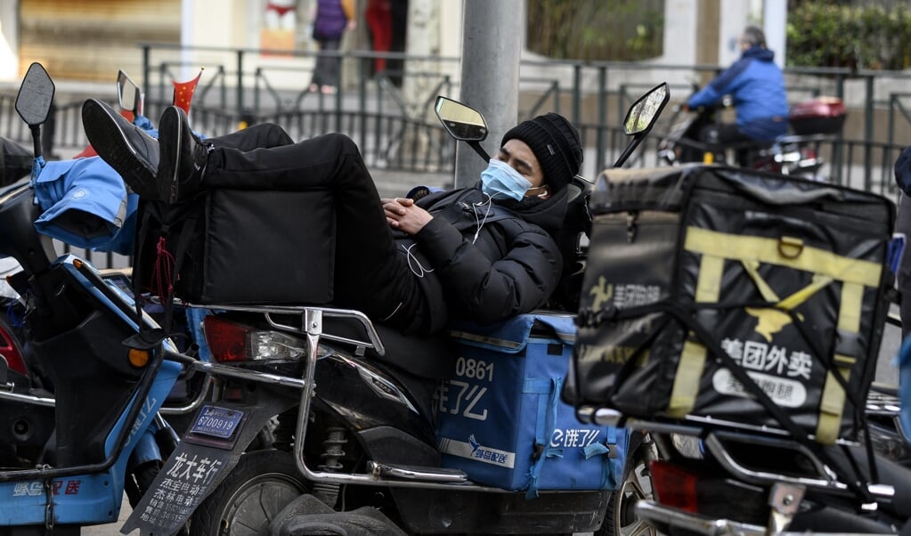 Een koerier in Shanghai rust uit terwijl hij op een nieuwe bezorgorder wacht. Meer mensen werken meer dan 55 uur per week. (beeld afp / Noel Celis)
