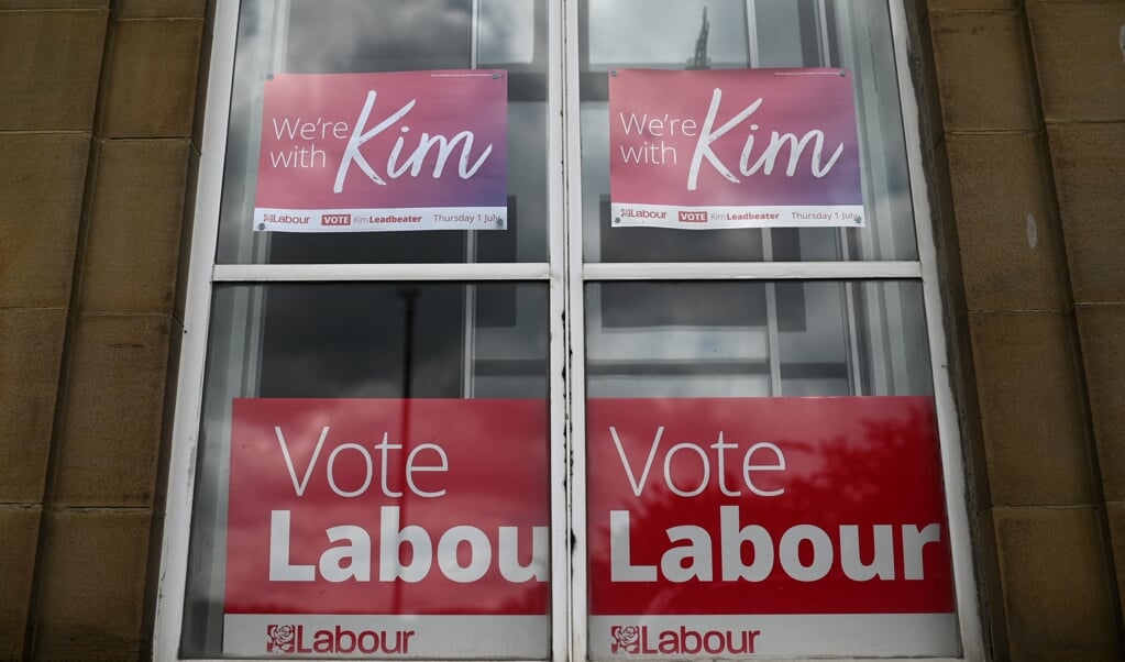 Een Labour-aanhanger heeft voor haar raam in Batley posters opgehangen voor kandidaat Kim Leadbeater, zus van de vermoorde politica Jo Cox. In het arbeidersstadje woedt een felle stembusstrijd op links. (beeld afp / Oli Scarff)