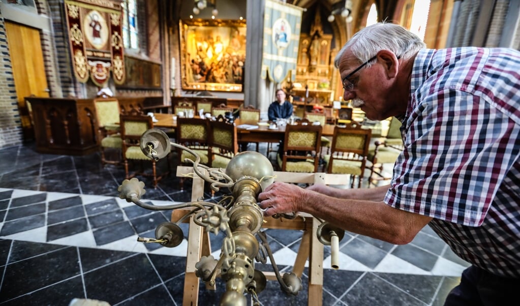 In de Sint Laurentiuskerk is Kees Pater bezig een oude kroonluchter op te kalefateren. (beeld Maarten Boersema)
