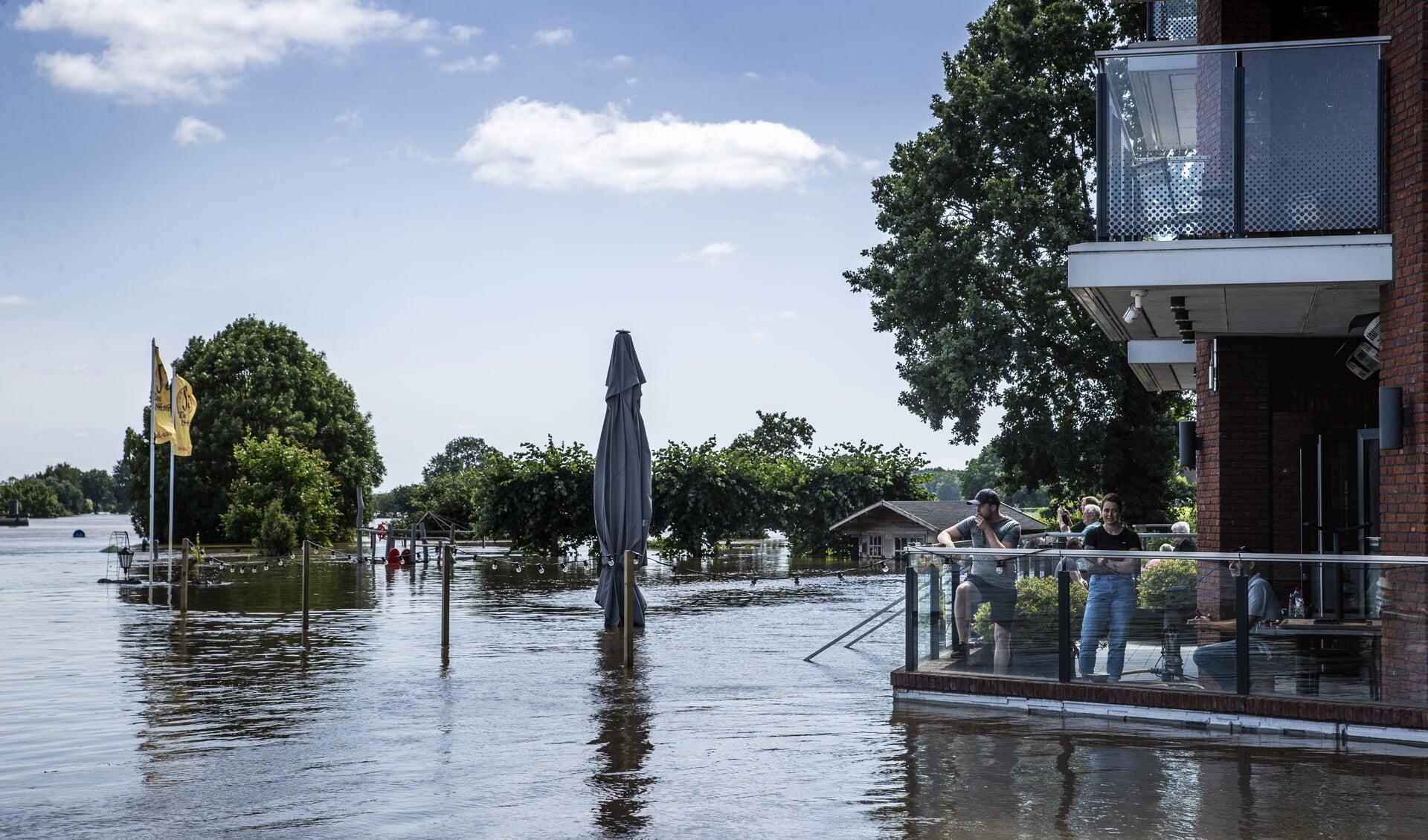 Bewoners van Broekhuizen kijken vanaf een terras naar het hoge water in de Maas. Limburg is getroffen door overstromingen.