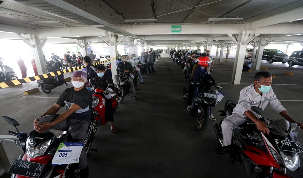 Motorrijders staan op een parkeerplaats bij een ziekenhuis in Jakarta in de rij voor een vaccinatie. In de stad sterven mensen op straat aan corona. (beeld epa / Bagus Indahono)