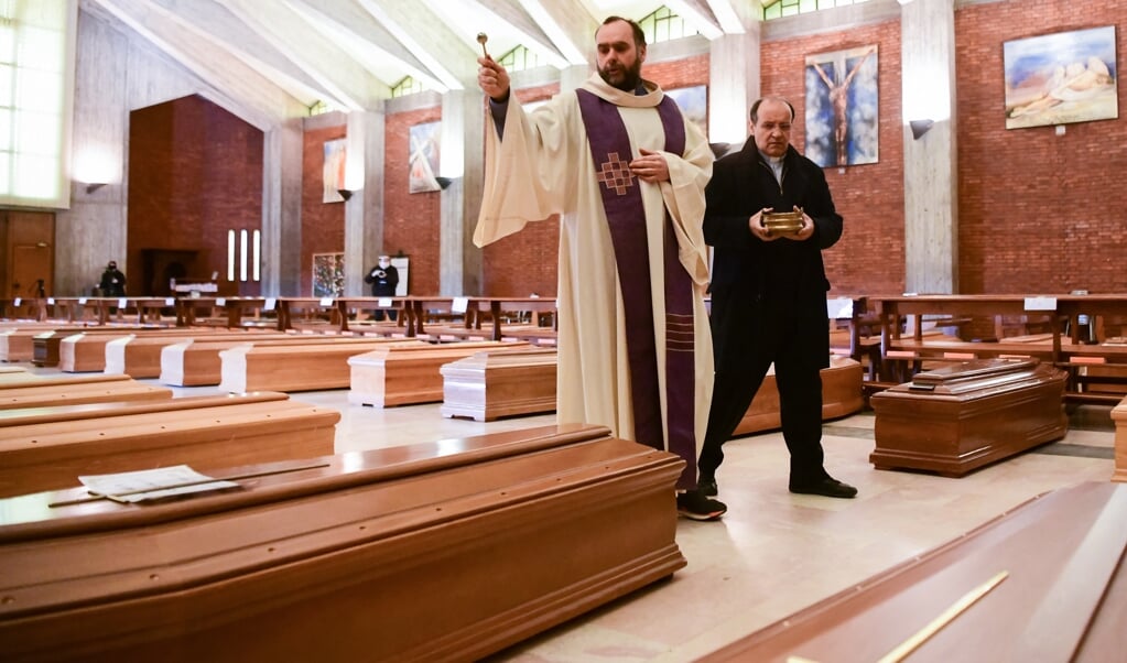 Priesters Marcello Crotti en Mario Carminati besprenkelen op 28 maart 2020 de doodskisten in de San Giuseppe-kerk in Seriate, net buiten Bergamo. (beeld afp / Piero Cruciatti)