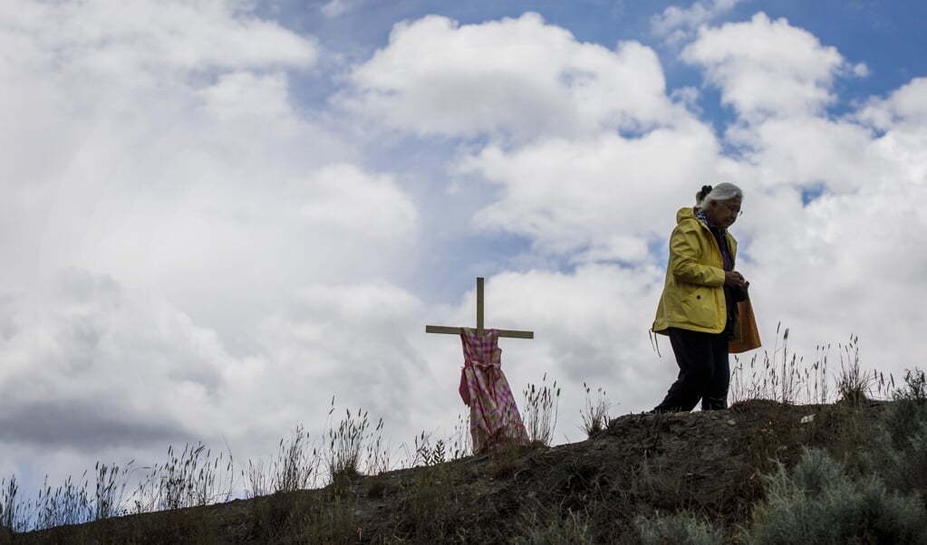 Een kruis met een meisjesjurk herinnert bij het voormalige internaat in Kamloops aan de 215 anonieme kinderen die er op het grondgebied begraven liggen. (beeld afp / Cole Burston)