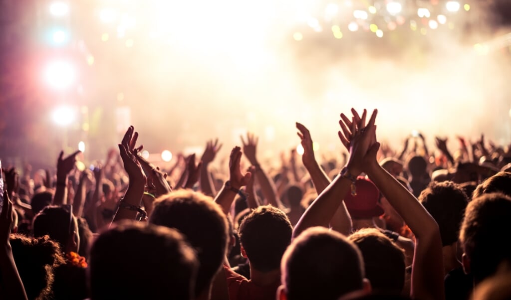 Audience with hands raised at a music festival and lights streaming down from above the stage. Soft focus, blurred movement. (beeld Bernard Bodo)