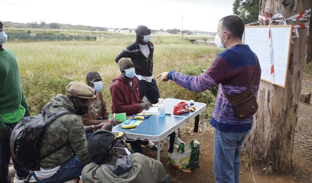 Buiten het migrantenkamp Las Raíces op Tenerife geeft een vrijwilliger Spaanse les aan een handvol jonge mannen. (beeld Lex Rietman)