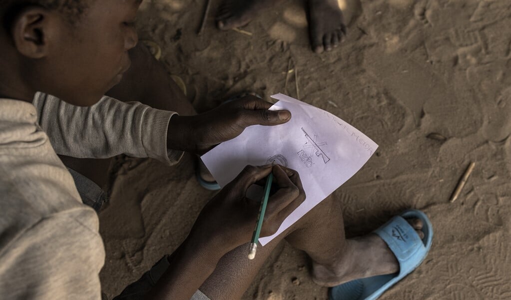 Een jongen tekent een symbool voor 'geen wapens' in een opvangkamp voor gevluchte personen in Mozambique.   (beeld afp / John Wessels)