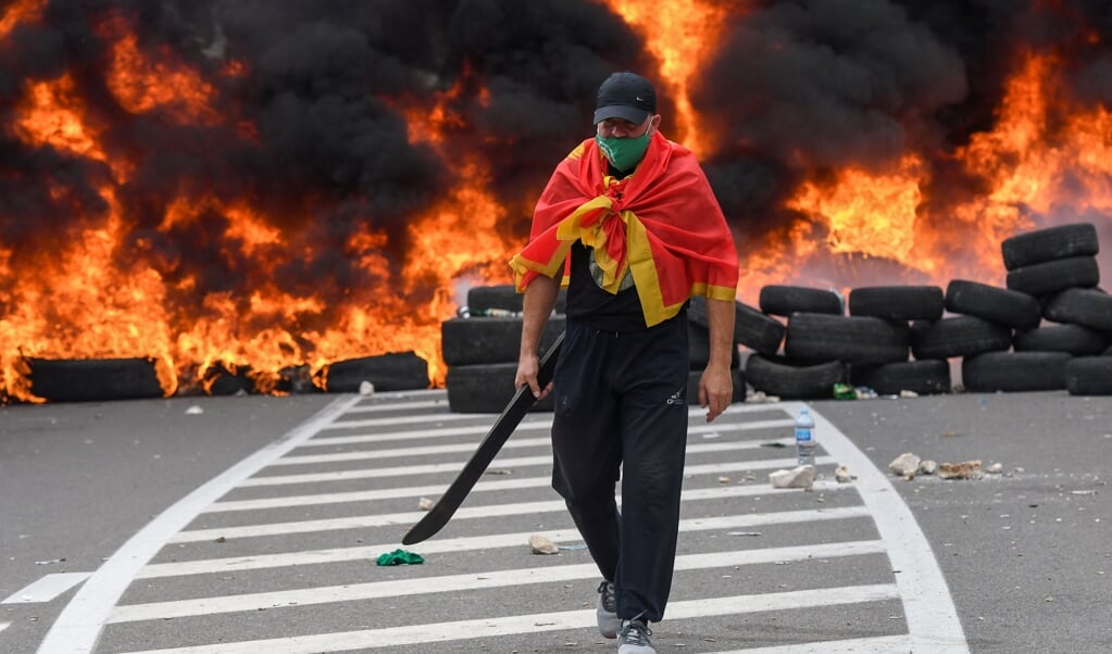 Een man met omgeslagen Montenegrijnse vlag loopt weg bij een wegbarricade vol brandende autobanden in het land. De inhuldiging van de Servische kerkleider Joanikije heeft veel Montegrijnen woedend gemaakt. (beeld afp / Savo Prelevic)