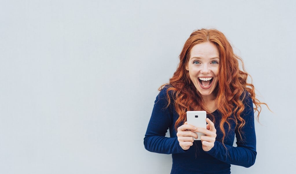 Vivacious young woman laughing at a good joke as she stands against a white wall with copy space holding a mobile (beeld contrastwerkstatt)