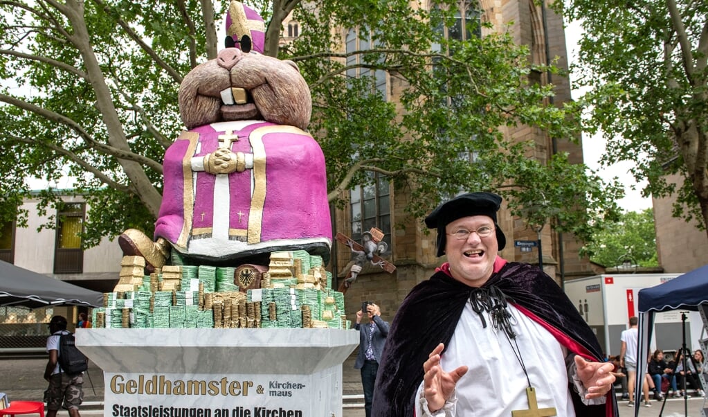 Met een ‘geldhamster’ protesteert een betoger tegen de Duitse kerkbelasting, tijdens de Kirchentag in Dortmund in 2019. (beeld ekd)