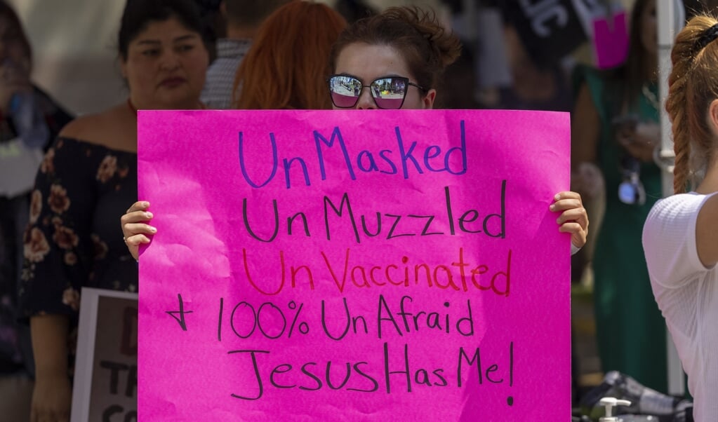 Een vrouw in Los Angeles houdt een protestbord omhoog waarop staat dat zij niet gevaccineerd hoeft te worden of een masker hoeft te dragen, omdat Jezus haar zal beschermen tegen het coronavirus.  (beeld afp / David McNew)