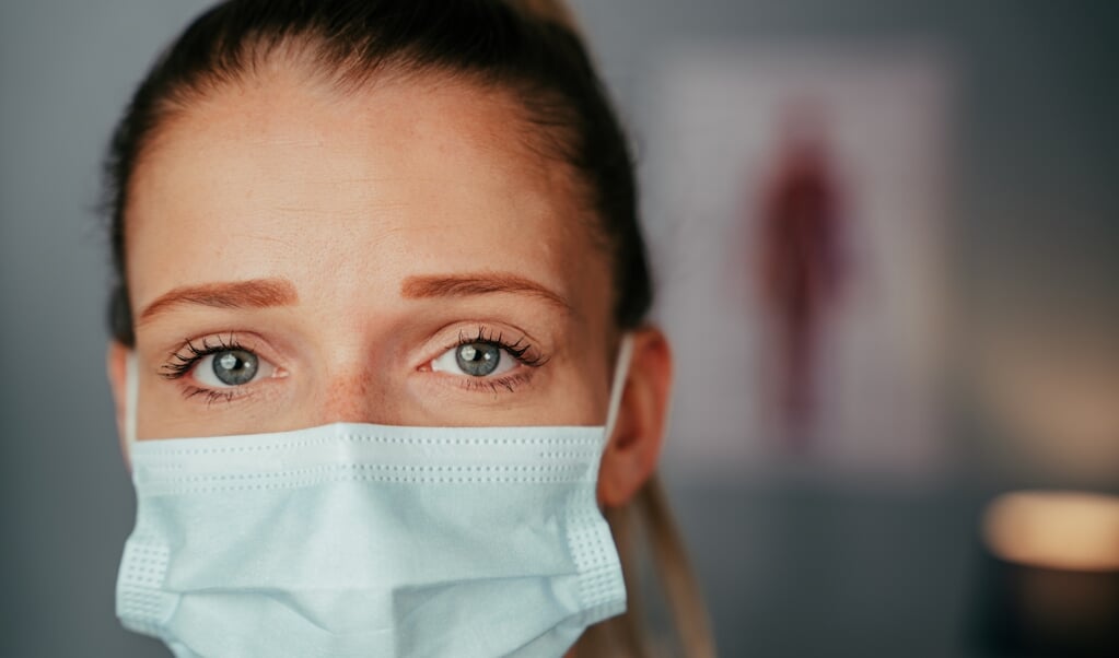 Close up caucasian female nurse standing in doctors office wearing surgical mask. High quality photo  (beeld Getty Images/iStockphoto)