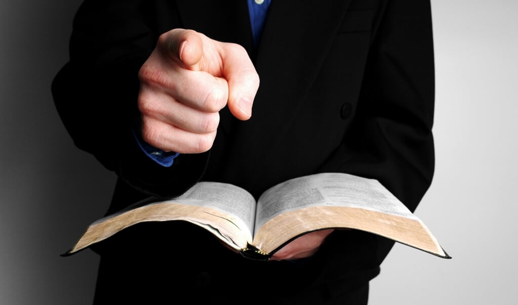 High contrast shot of a minister holding an open Bible and pointing at you. (beeld getty images / istock)