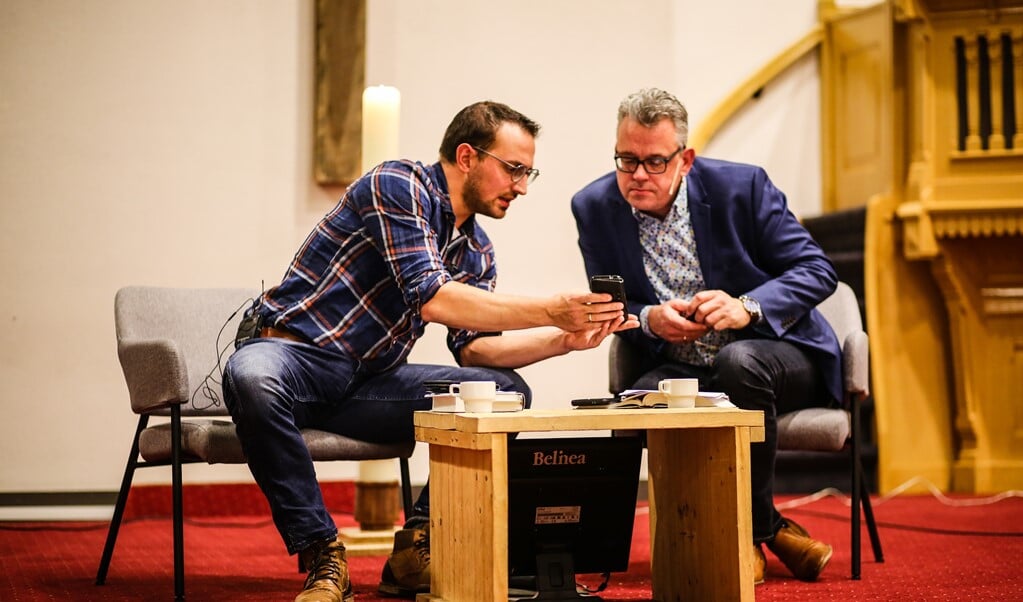 Predikanten Tim Waalewijn (l.) en Roel Prins overleggen, terwijl de thuiskijkers van 'Koffie met de Bijbel' een filmpje te zien krijgen. (beeld Maarten Boersema)
