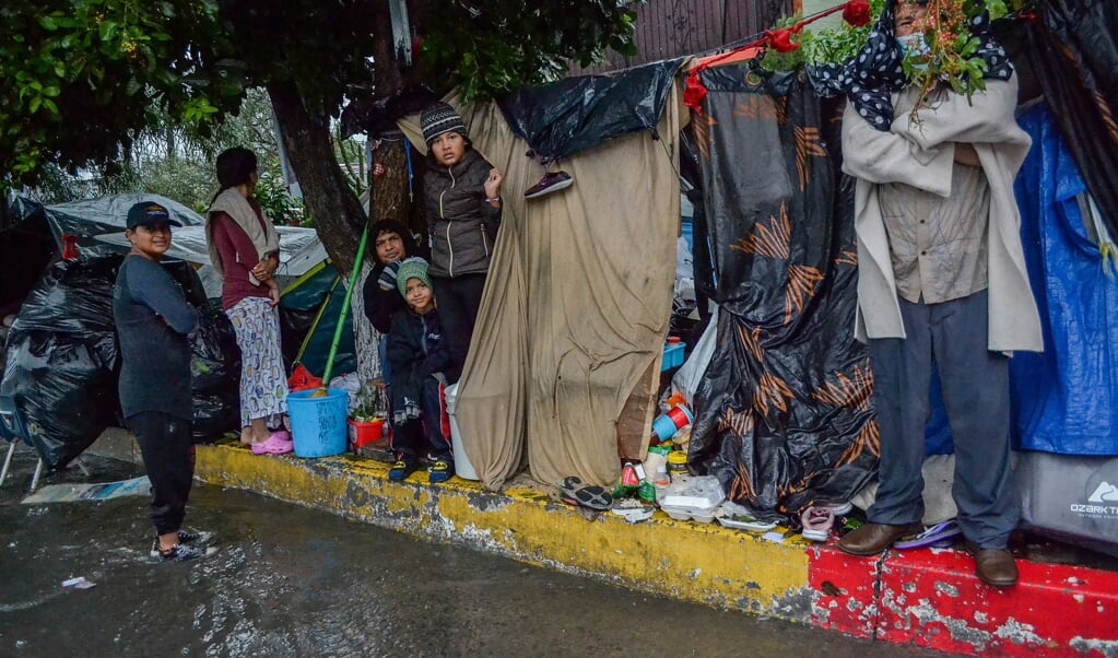 Migranten in de Mexicaanse stad Tijuana proberen te schuilen voor de hevige regen. In december vorig jaar werd de stad geteisterd door forse regenval.   (beeld epa / Joebeth Terriquez)