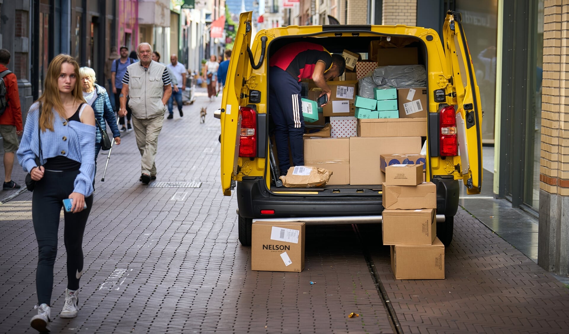 Pakketbezorgers leveren hun pakketjes af in een winkelstraat.