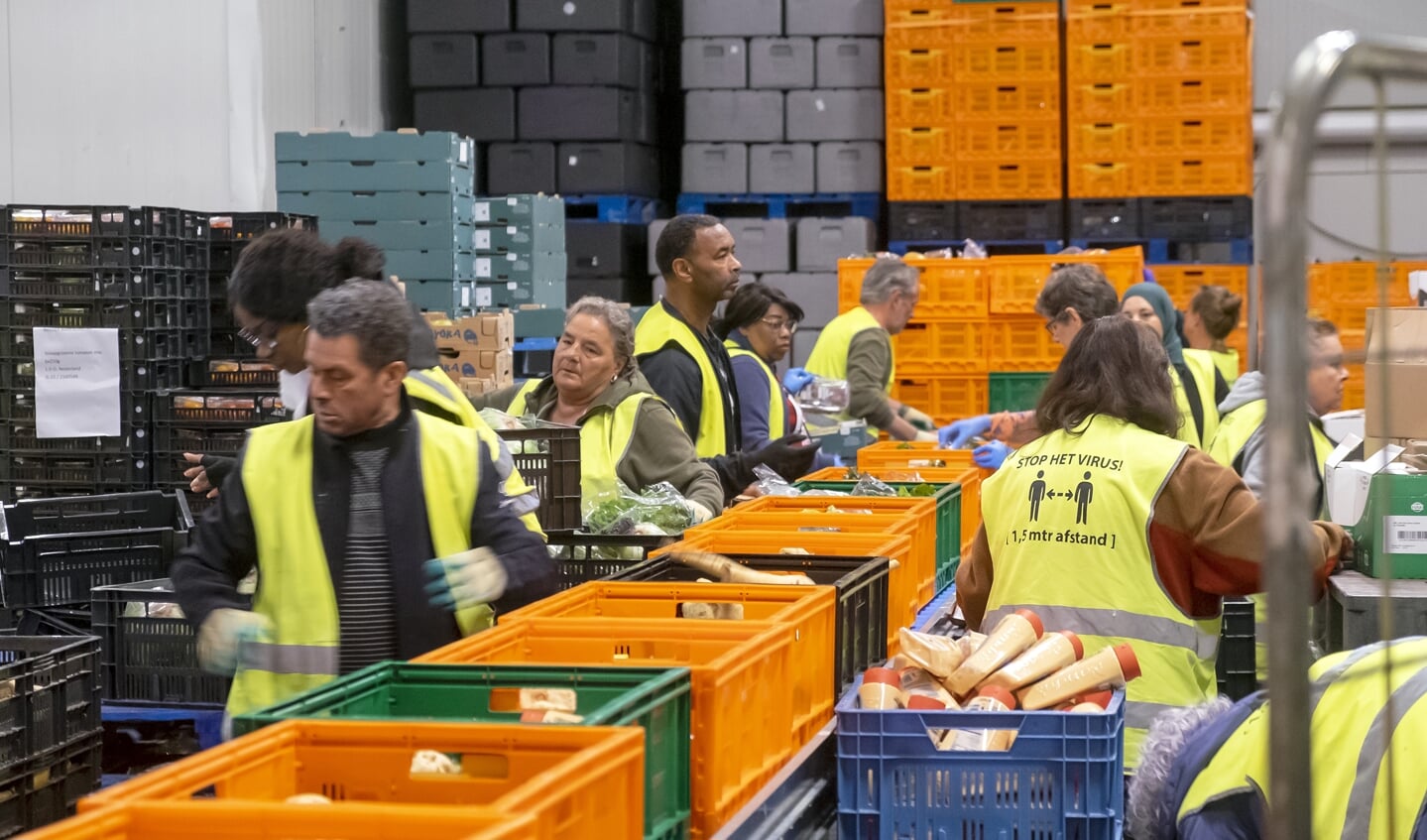 Medewerkers van de Voedselbank vullen kratjes met voedsel. Kerken in Ede hebben bezoekers van de voedselbank een extraatje uitgedeeld om hen in deze dure tijd te ondersteunen.