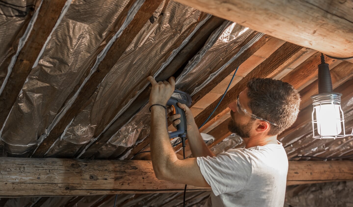 Een man isoleert het dak van zijn huis. Voor een gemiddelde hoekwoning ben je voor dakisolatie 1700 euro kwijt aan materiaal.