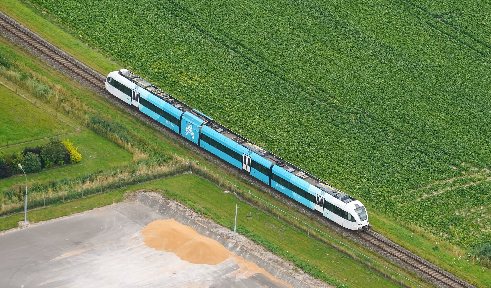 Een blauw met witte Arriva trein rijdt door de weilanden van Groningen in een groen landschap ter hoogte van Uithuizen.
