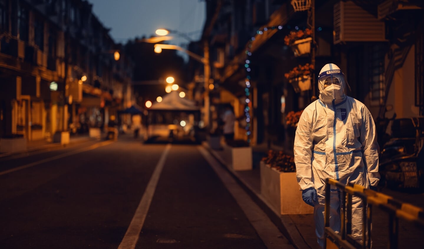 Een politieagent in beschermende kleding houdt de wacht in een straat in Shanghai.