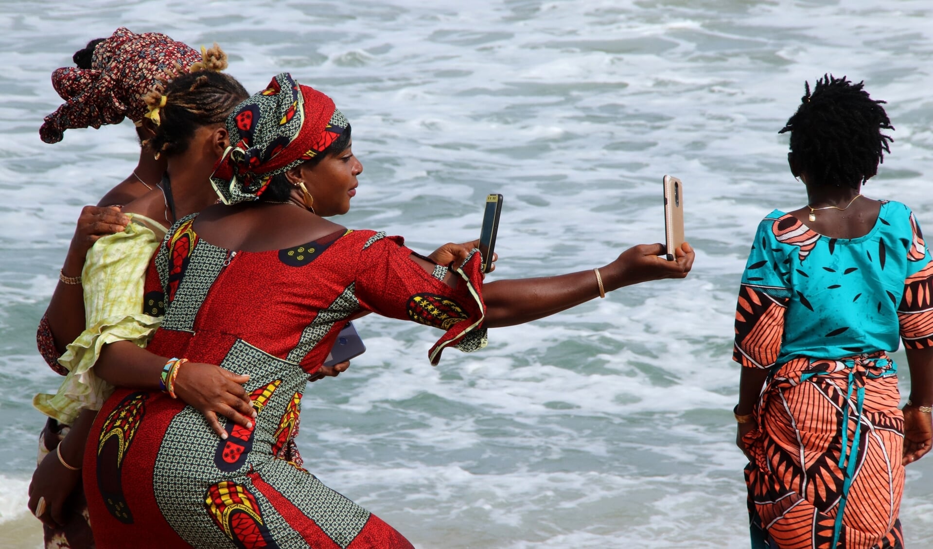 Vrouwen in traditioneel Afrikaanse kleding nemens selfies aan het strand in Togo. 90 procent van de Togolezen heeft een telefoon.