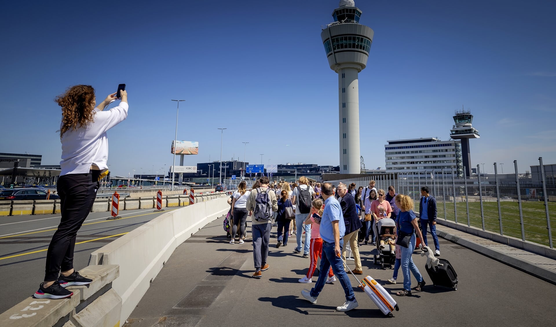 Reizigers wachten in lange rijen buiten op Schiphol. Zij mogen alleen de vertrekhallen in als hun vlucht binnen vier uur vertrekt. Afgelopen weken ontstond drukte op Schiphol; veel vakantiegangers en weinig personeel.