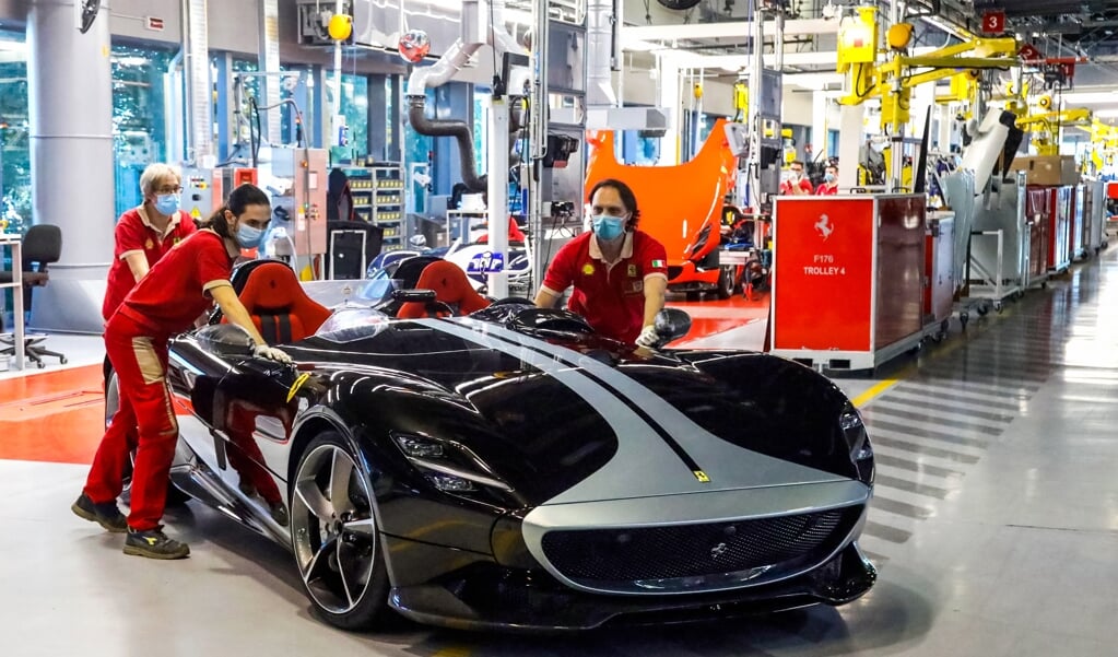 Arbeiders van autofabrikant Ferrari duwen een Monza SP2 V12 sportwagen voort.  (beeld afp)