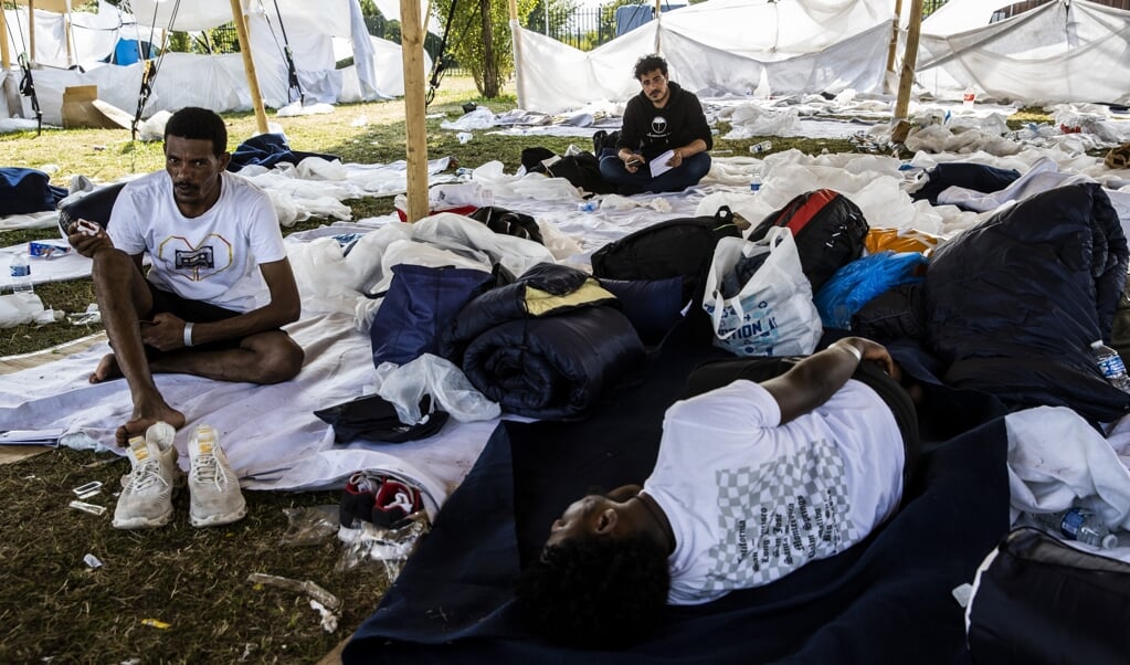 Asielzoekers wachten in de schaduw bij het overvolle aanmeldcentrum. Door grote drukte staan asielzoekers uren in de hitte tot ze zich kunnen aanmelden.  (beeld anp / Vincent Jannink)